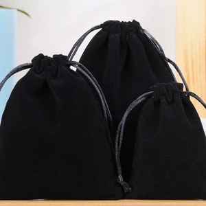 Three sizes of black velvet drawstring jewelry bags displayed on a wooden base
