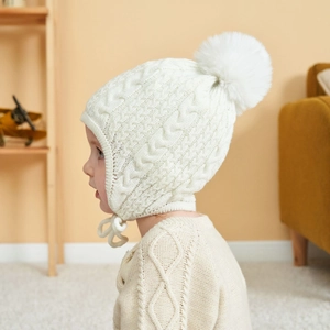 Detail of baby knit hat with cable pattern and white pompom on a cozy background