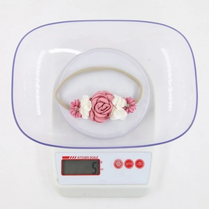 Detail showing baby floral headband with fabric flowers and pearls on electronic scale
