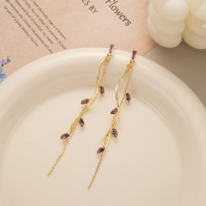 Detailed view of long gold tassel earrings with purple leaf crystals on a white ceramic dish