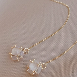 Minimalist gold plated drop earrings with translucent cat eye stones on beige fabric