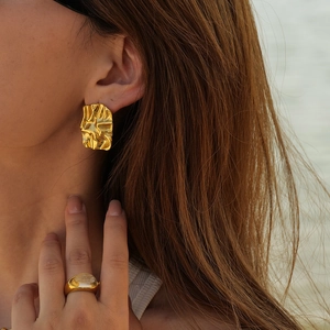 Detail of gold irregular textured stud earrings and bold ring worn by a model outdoors
