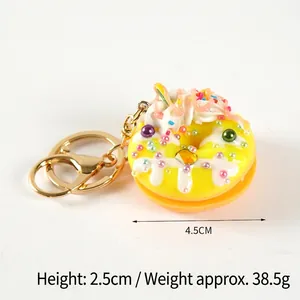 Bright yellow resin donut keychain with white cream and colorful sprinkles on a white base