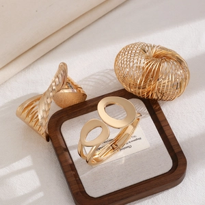 Detail of three gold metallic textured bangle set with spiral and geometric hollow designs
