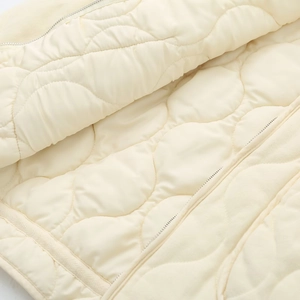 Macro shot of wavy quilted cream jacket showing fine stitching and smooth zipper detail