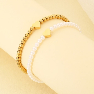 Close-up of elegant gold bead and pearl heart bracelets on a beige background