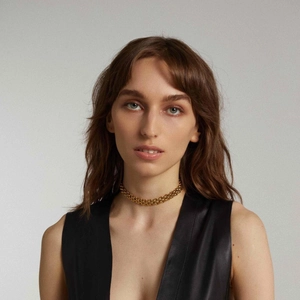 Detail shot of chunky gold braided chain necklace on model wearing black leather vest
