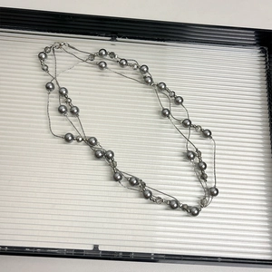 Multi-layer long necklace featuring grey pearls and silver-tone chains on a white tray