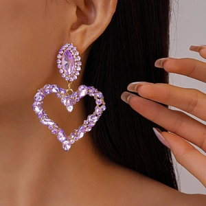 Detail view of large purple crystal heart earrings with gold metal and diamond accents