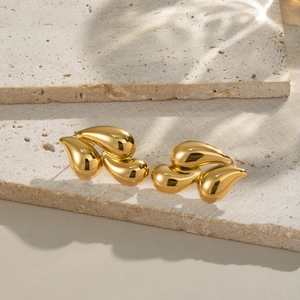 Polished 18K gold teardrop earrings on a beige stone surface with natural light