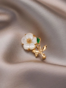 Macro detail of floral brooch with shell petals and green zircon leaf on silk