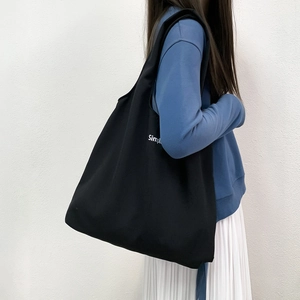 Détail du grand sac cabas noir en toile avec imprimé Simpl porté par un mannequin