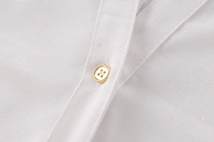 Detail of white linen blend shirt fabric showing a golden button and fine stitching