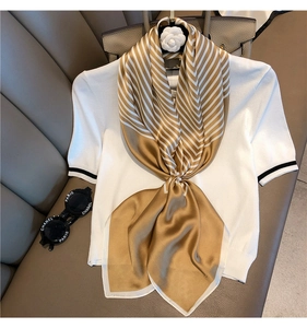 Detail of elegant gold and white striped silk scarf draped on white knit top
