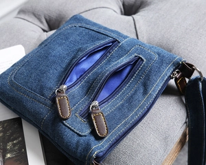 Detailed close-up of blue denim shoulder bag with heavy stitching and double zip pockets