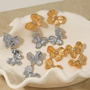 Elegant gold and silver bow earrings with zircon stones displayed on shell tray