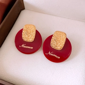 Macro view of vintage gold-plated earrings with red circular base and Nuance text