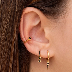 Elegant gold earrings set with black stones shown on ear, including cuffs and dangles