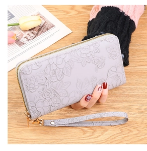 Detail view of light grey long wallet featuring embossed floral design and golden hardware
