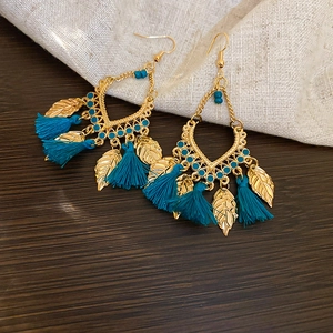 Detailed shot of Bohemian teal tassel earrings with golden leaves on a rustic wood surface