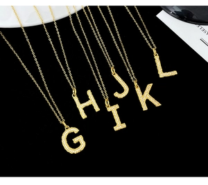Close-up of golden letter pendants G to L with shimmering white crystals on black velvet