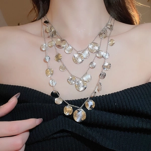 Detail of layered silver necklace with hammered round discs on a black knit top
