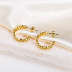 Detailed view of gold C-ring earrings with beaded texture on white stone and silk background