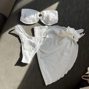 Three-piece white textured bikini set with bandeau top, briefs, and matching sarong skirt