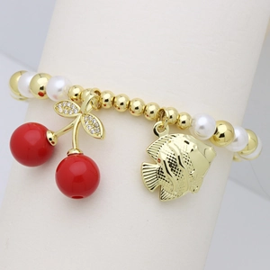 Detail of beaded pearl bracelet with red cherry charm and golden tropical fish pendant
