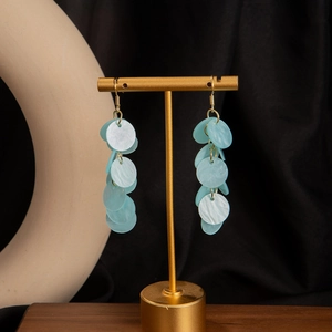 Close-up of light blue layered shell tassels on a golden earring hook displayed on a stand