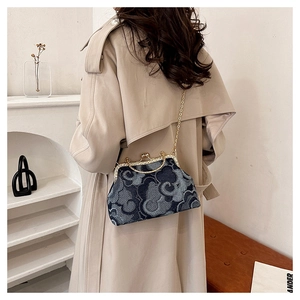 Detail of a denim handbag with cloud patterns and a gold chain strap on a trench coat