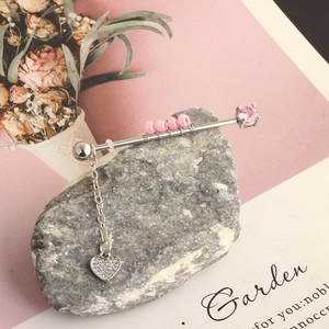 Detail of silver industrial piercing jewelry with pink gems and heart pendant on gray stone