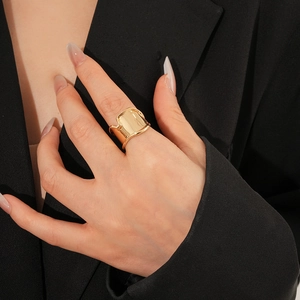 Close-up of a wide gold irregular wavy ring worn by a model in a black suit