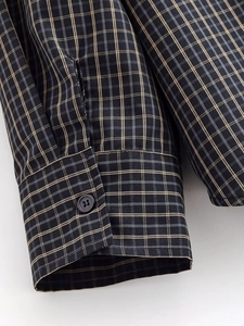 Gros plan sur la couture double et le bouton unique d'une chemise grise à carreaux