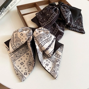 Close-up of silk bow hair clips with vintage paisley patterns in black and beige colors
