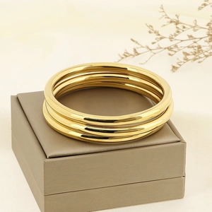 Detailed view of three polished gold stainless steel bangles set on a jewelry box