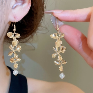 Macro detail of gold flower earrings showing brushed metal texture and pearl drop