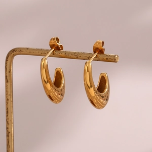 Macro detail of high-polish gold hook earrings displayed on a metal jewelry stand
