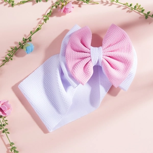 Close-up of pink and white layered bow headband with textured fabric on a floral background