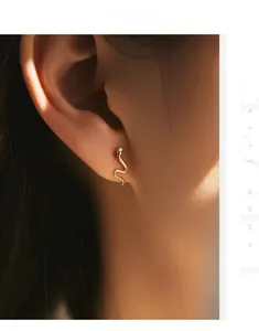 Macro shot of minimalist gold snake earrings with a sparkling diamond head on earlobe