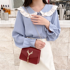 Red leather shoulder bag with gold deer tassel chain shown on a model in outdoor setting
