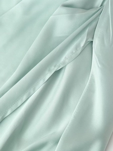 Dettaglio del tessuto satinato verde menta con eleganti drappeggi e texture setosa