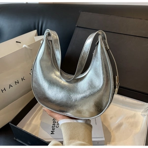 Detail of silver crescent shoulder bag featuring glossy metallic finish and sleek zipper