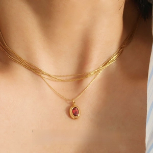 Close-up of a layered gold chain necklace featuring an oval dark red gemstone pendant