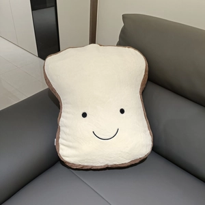 Soft plush toast pillow with cute smiley face embroidery on a leather sofa