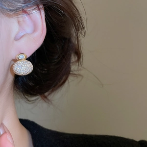 Close-up of a gold-plated earring with a round zircon stud and pavé sphere pendant