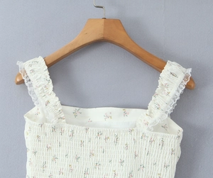 Close-up van een gebloemde gesmokte top met witte kanten bandjes op houten hanger
