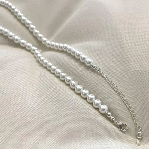 Macro detail of round white pearl necklace with silver lobster clasp and extension chain
