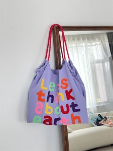 Detail of purple canvas tote bag with embroidered letters and red woven handles