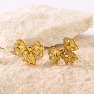Elegant gold-plated stainless steel bow earrings displayed on a natural light stone base